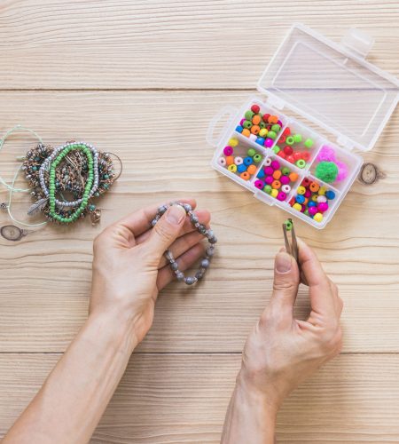 close up hand holding beads with tweezers wooden table